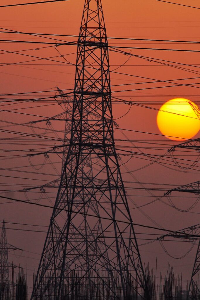 High-tension power lines silhouetted by a dramatic and colorful sunset sky, representing energy distribution.