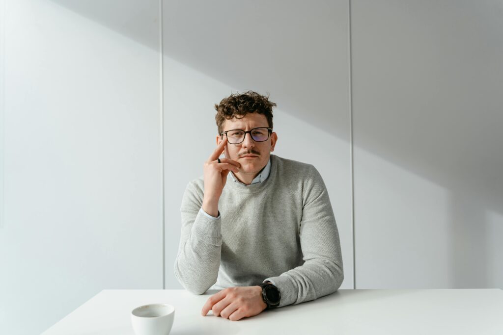 pexels photo 7255383 7255383 Man in glasses sitting at a bright and minimalist office desk, exuding a calm and focused demeanor.